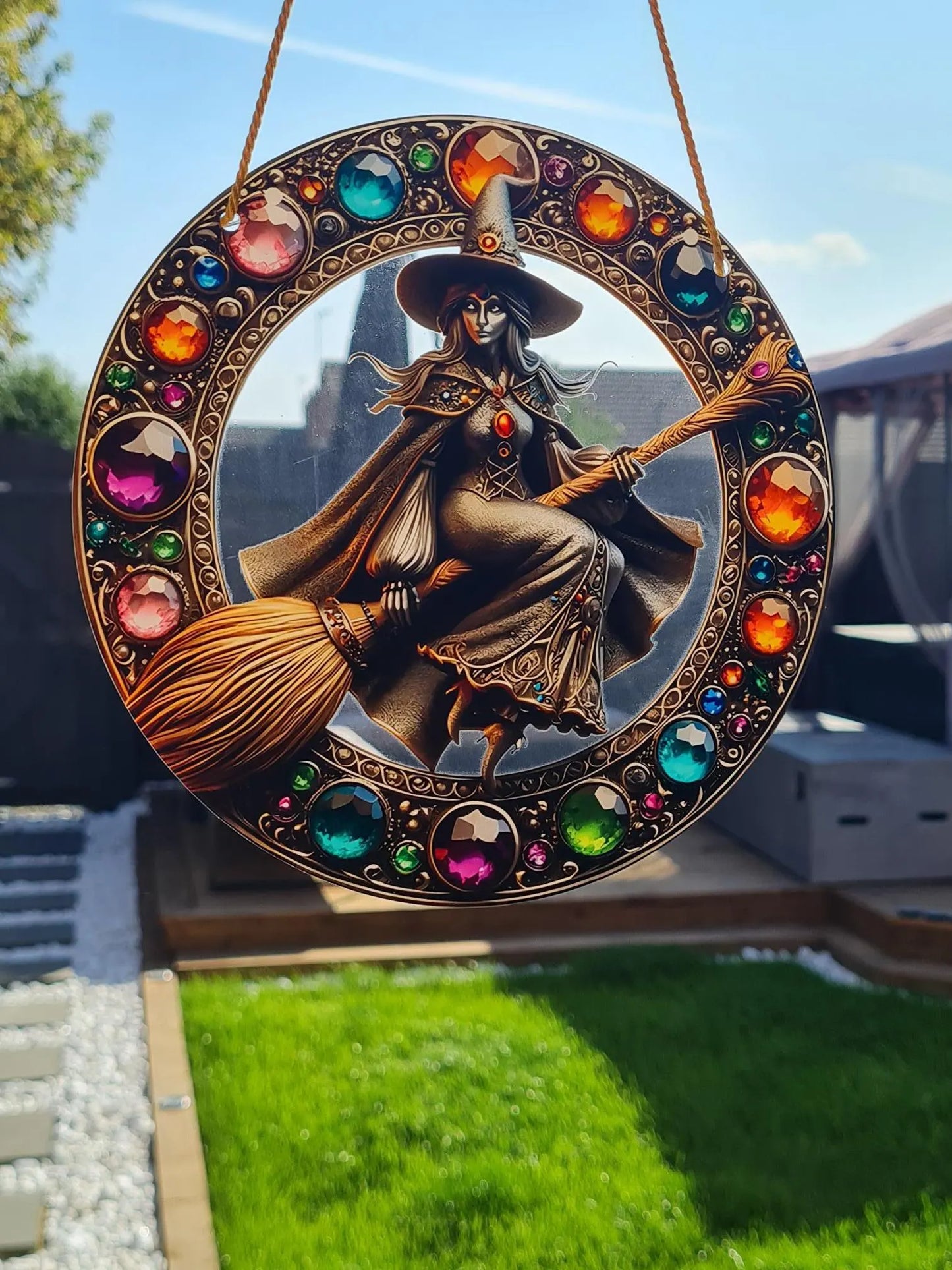Gothic stained glass sun catcher featuring an adorable witch on a broomstick within a crescent moon adorned with bat wings and vibrant autumnal leaves. Perfect for adding a spooky yet charming touch to any window or garden decor.