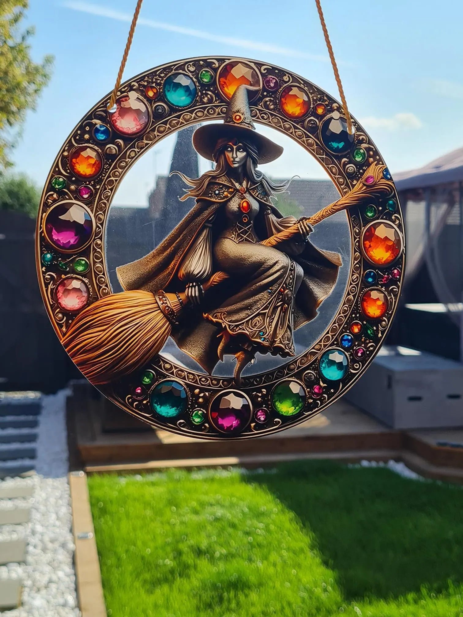 Gothic stained glass sun catcher featuring an adorable witch on a broomstick within a crescent moon adorned with bat wings and vibrant autumnal leaves. Perfect for adding a spooky yet charming touch to any window or garden decor.