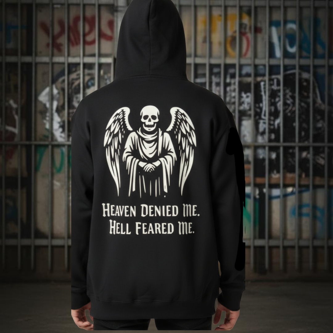 Black hoodie with a winged skeleton design and text against a graffiti-covered wall. heaven denied me hell feared me black gothic hoodie, alternative streetwear